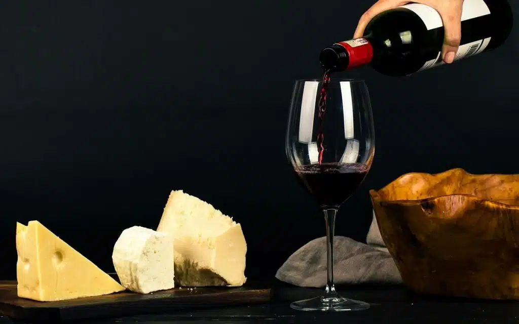 Ein Glas Rotwein, das eingegossen wird und verschiedene Stücke Käse